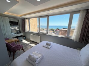 Une chambre d’hôtel avec un lit, un bureau, une chaise et une grande fenêtre donnant sur la ville.