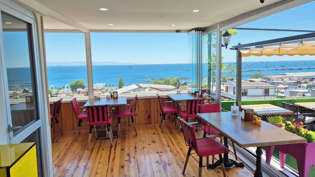 A restaurant with wooden flooring, red chairs, and large windows offering a view of the sea and cityscape. - Verseca Hotel (Istanbul)