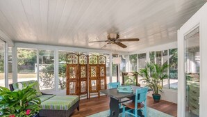 Un salón de sol con ventilador de techo, una mesa de comedor con sillas, un banco acolchado y un biombo decorativo.
