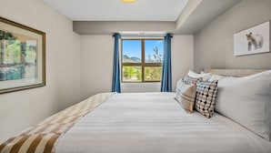 Une chambre avec un grand lit, une fenêtre donnant sur les montagnes, un lustre et un tableau encadré au mur.