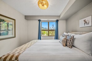 A bedroom with a large bed, a window with a view of mountains, a chandelier, and a framed picture on the wall.