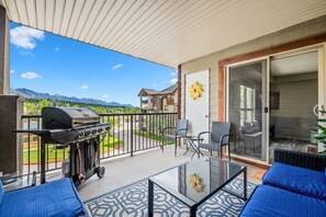 A balcony with a grill, outdoor furniture, and a view of mountains.