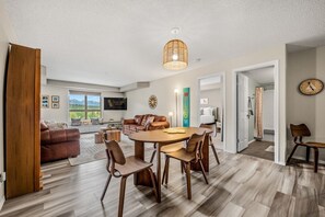 A modern living room with a dining area, a large window, and a flat-screen TV.