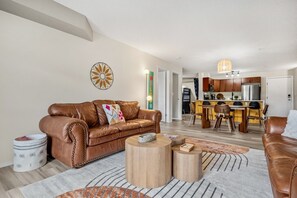 A modern living room with a brown leather sofa, a wooden coffee table, and a kitchen in the background.