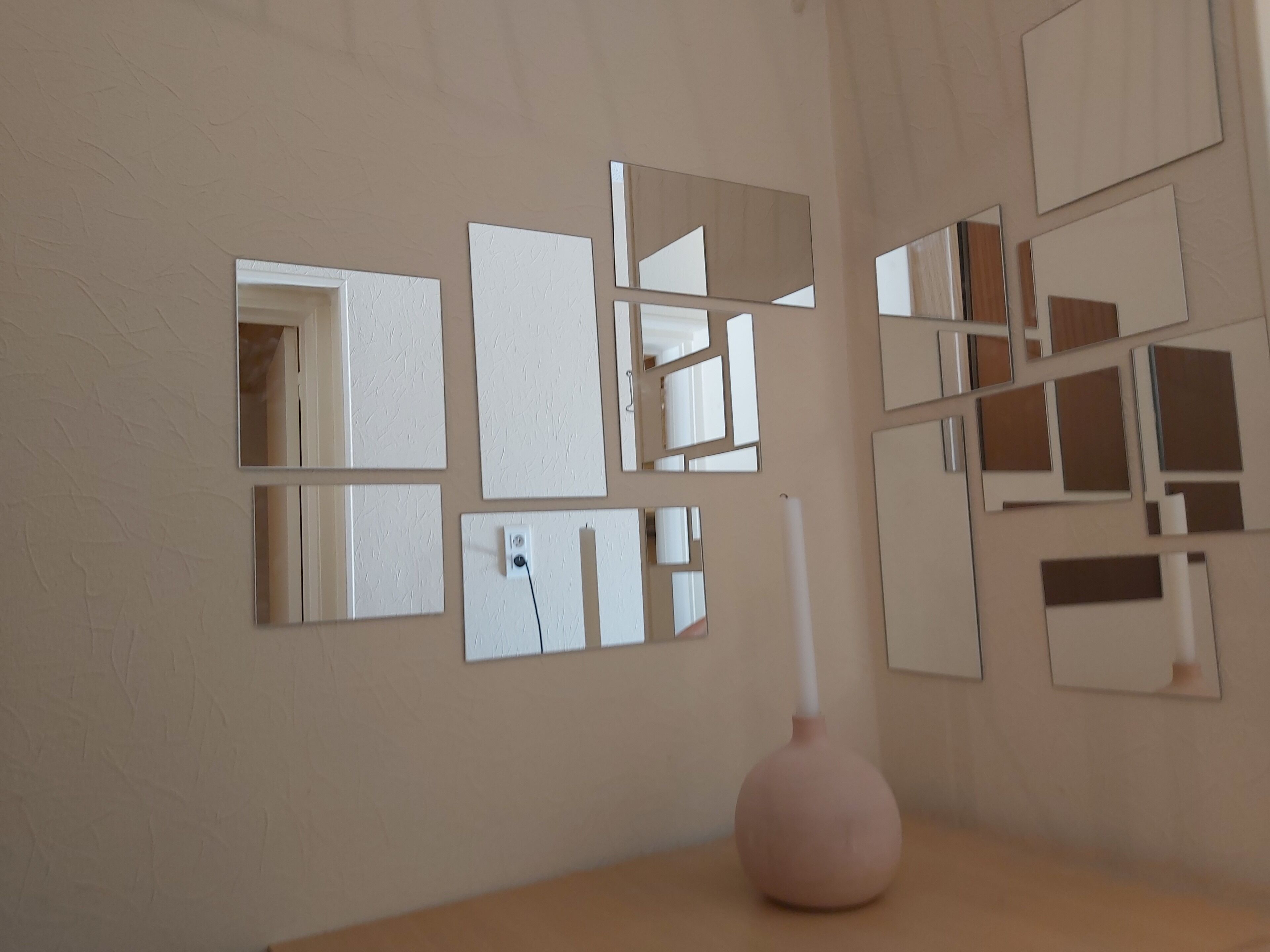 A wall with multiple mirrors and a vase.