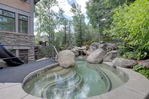 A hot tub surrounded by rocks and greenery, with a stone wall and a metal railing. - Snowmass Village Retreat Close to Slopes & Trails! (Snowmass Village)