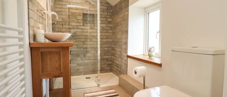 Un baño moderno con ducha de vidrio, tocador de madera, inodoro y ventana.