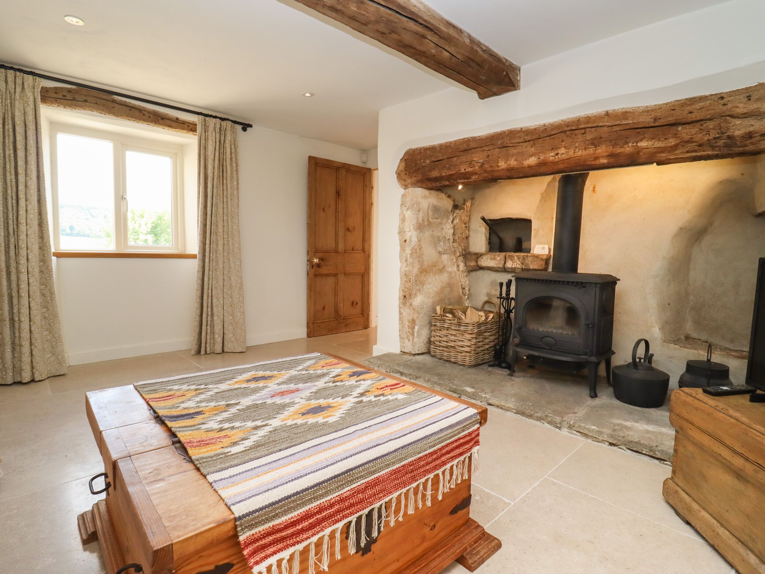A cozy room with a wooden bench, a stone fireplace, and a large window with curtains.