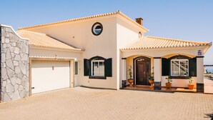 A two-story house with a tiled roof, a stone wall on the left, and a garage on the right. - Harmony (Air conditioning, kitchen, balcony, self-check-in, dishware and linens provided, privacy) (Ponta do Sol)