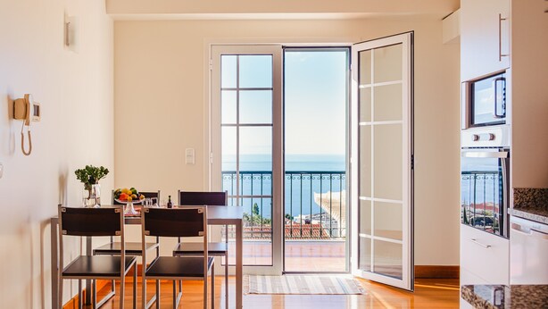 A modern kitchen with a view of the sea, a dining area with chairs and a table, and a sliding glass door leading to an outdoor balcony. - Harmony (Air conditioning, kitchen, balcony, self-check-in, dishware and linens provided, privacy) (Ponta do Sol)
