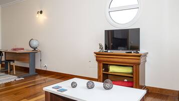 A living room with a white table displaying decorative items, a wooden TV stand with a flat-screen TV, a globe, and a statue on a desk.