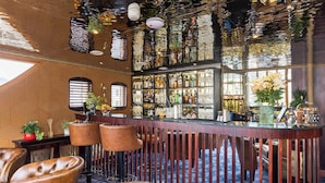 A bar area with leather chairs, a bar counter with bottles, and a patterned ceiling. - Ocean Mist Leith (Edinburgh)
