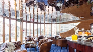A high-ceilinged lounge with leather seating, a bar area with breakfast items, and a city view through large windows. - Ocean Mist Leith (Edinburgh)