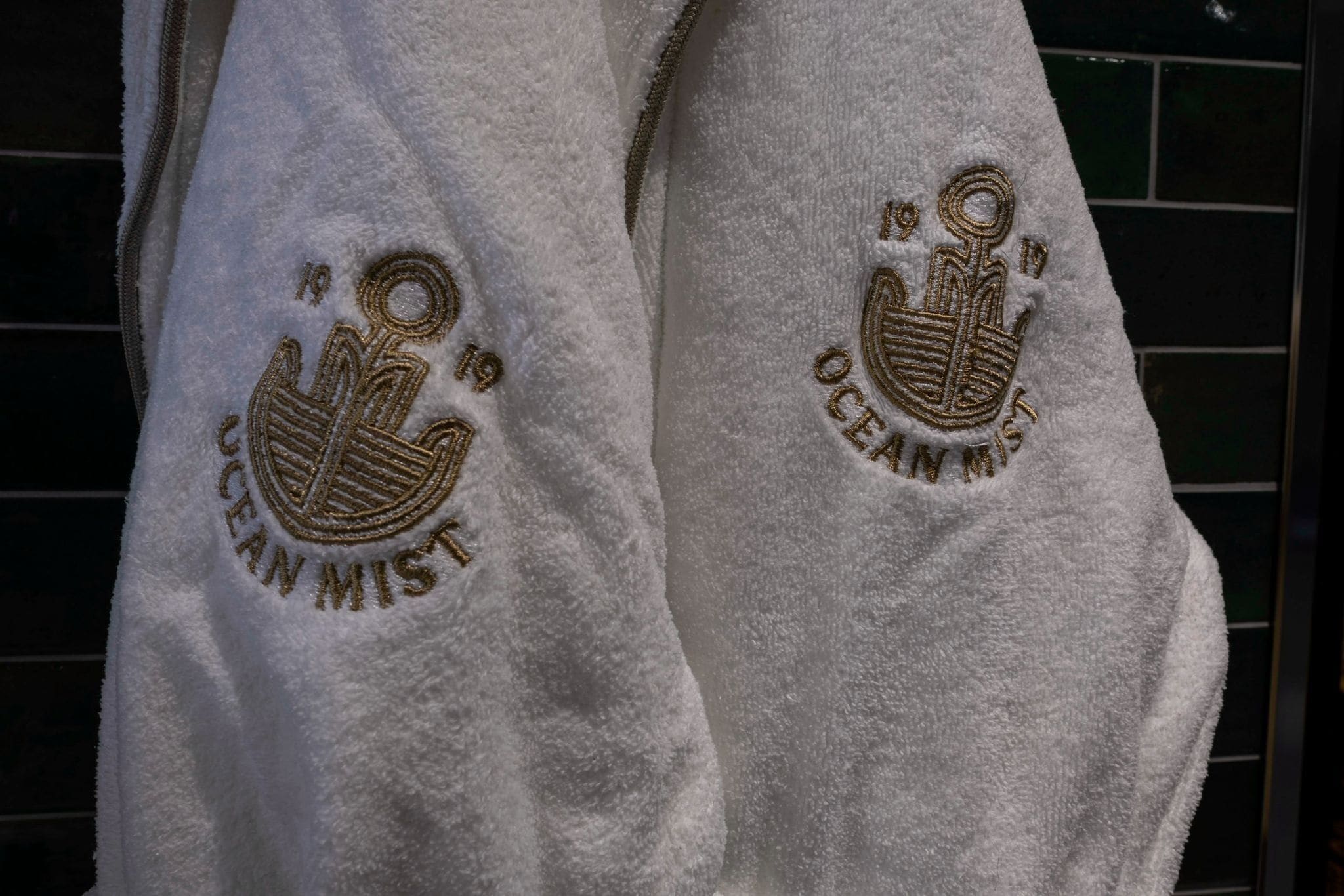 Toalla blanca con texto bordado y un emblema de corona, probablemente indicando un entorno de hotel o resort.