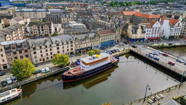 A large river with a boat docked at a pier, surrounded by historic buildings and a cityscape in the background.