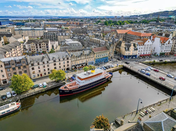 A large river with a boat docked at a pier, surrounded by historic buildings and a cityscape in the background. - Ocean Mist Leith (Edinburgh)