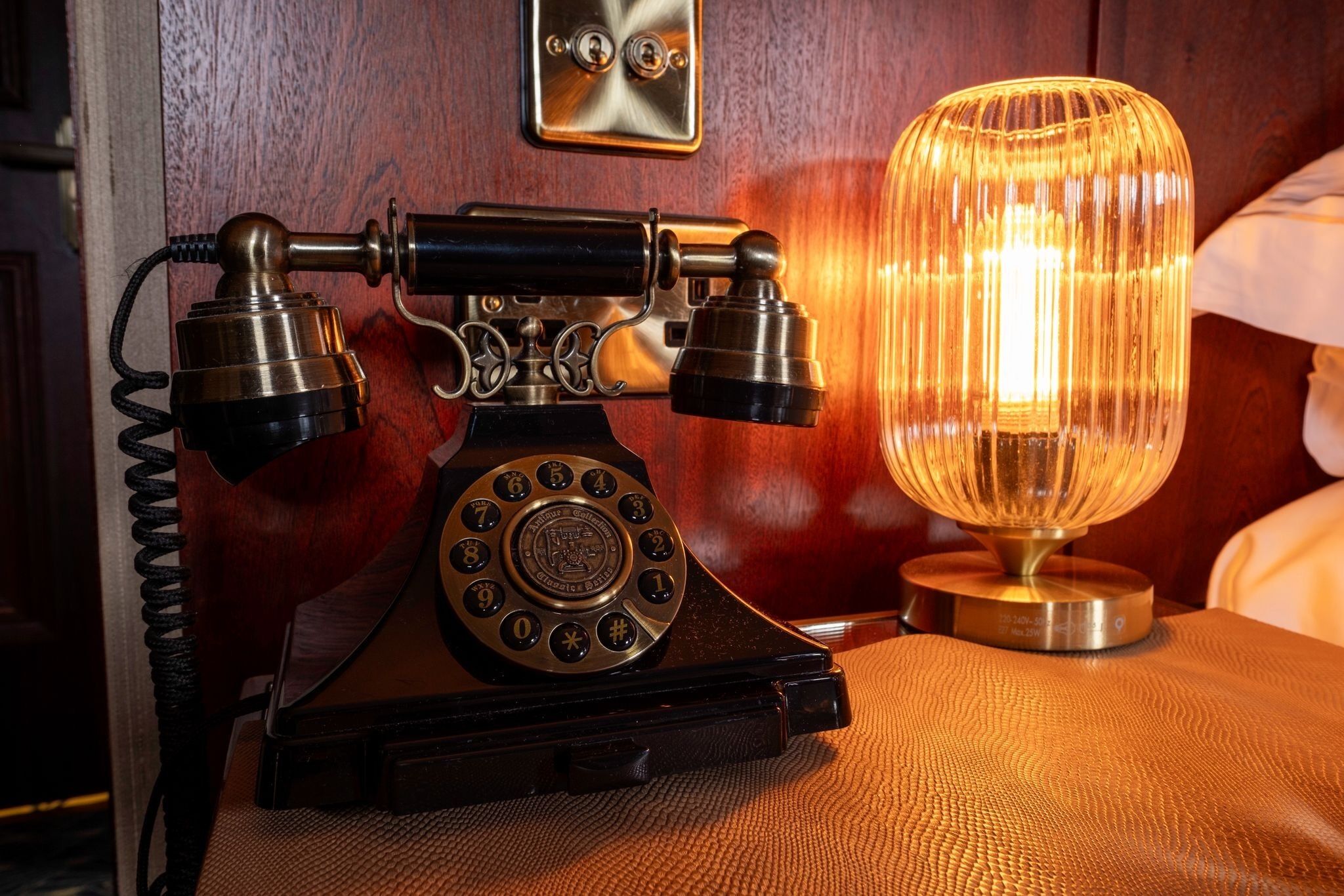 A vintage rotary dial telephone and a glass table lamp on a textured surface.