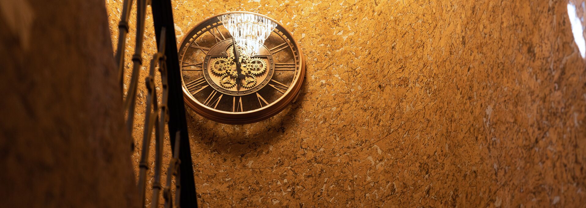 A brass clock with Roman numerals on a textured wall.
