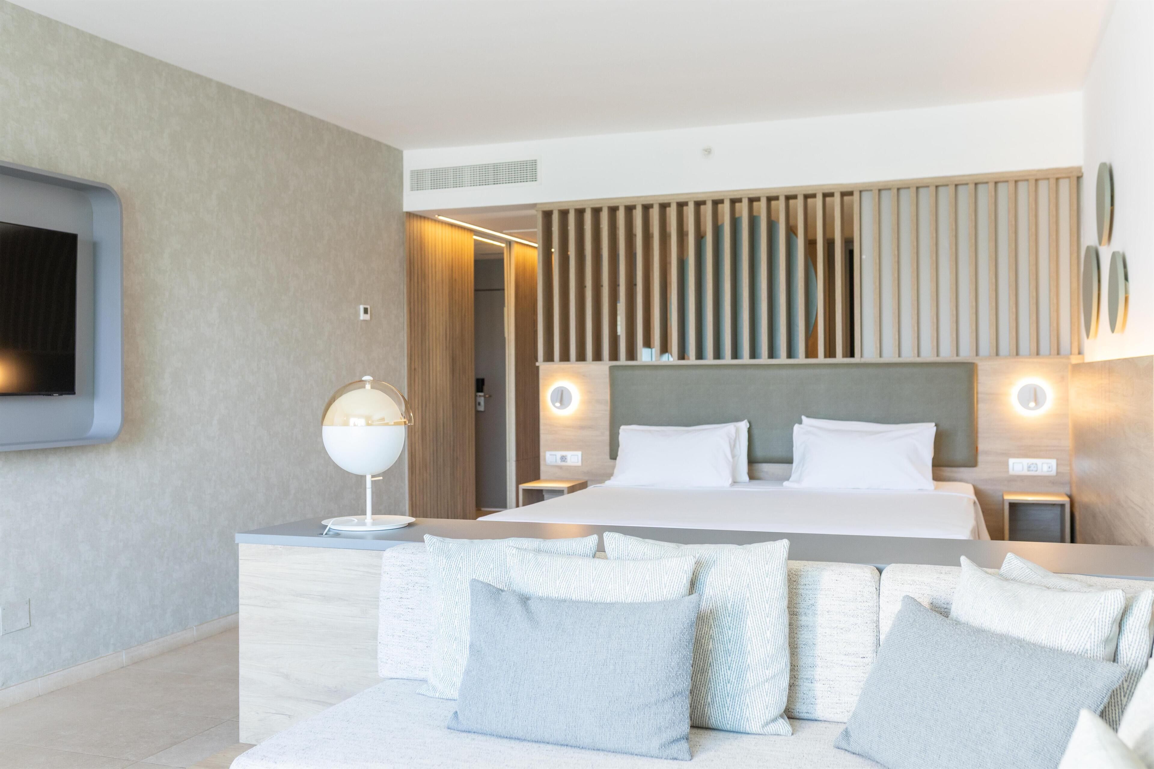 A modern hotel room with a large bed, bedside tables, a TV mounted on the wall, and a wooden panel design.