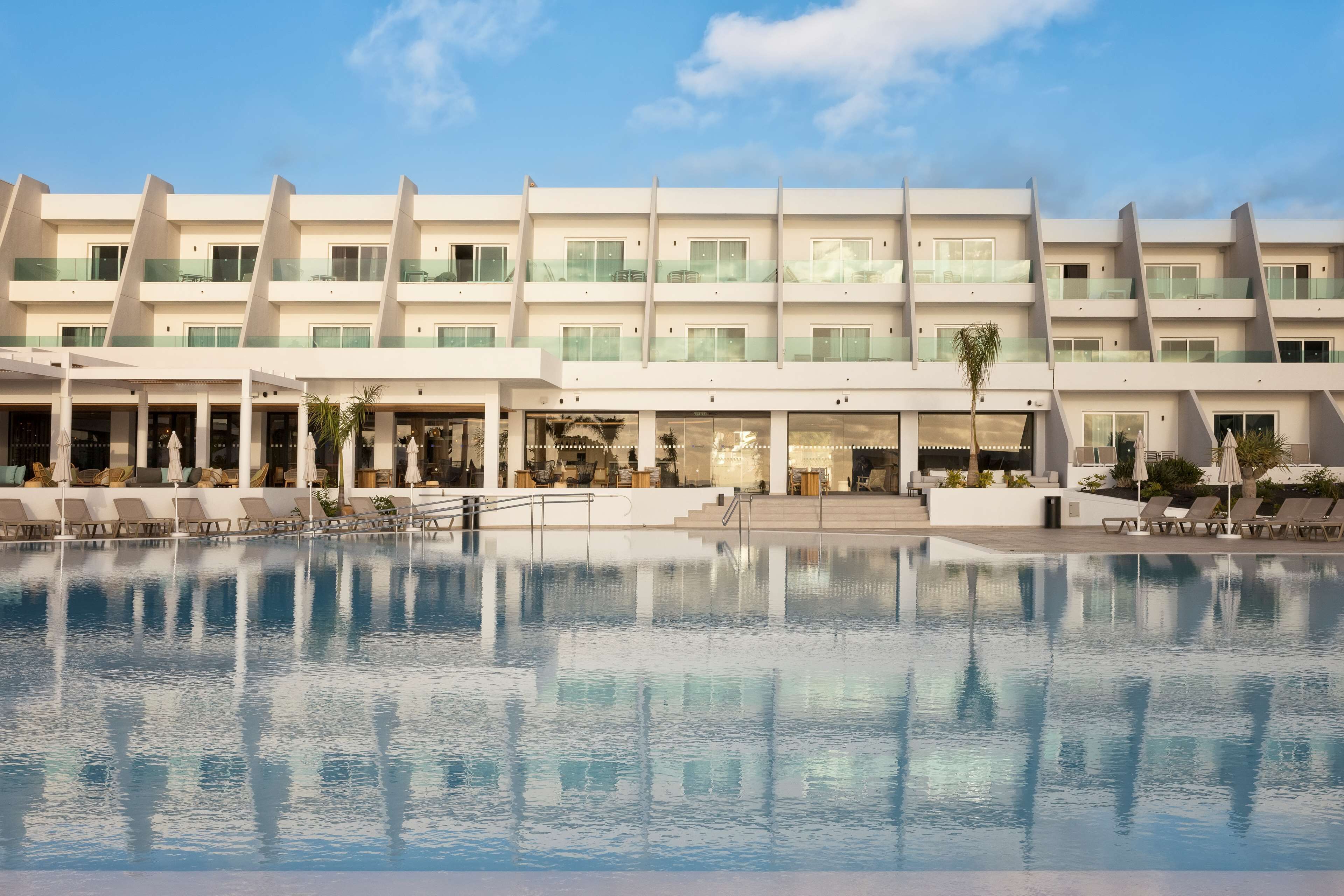 A modern hotel with a large pool, multiple balconies, and a clear sky.