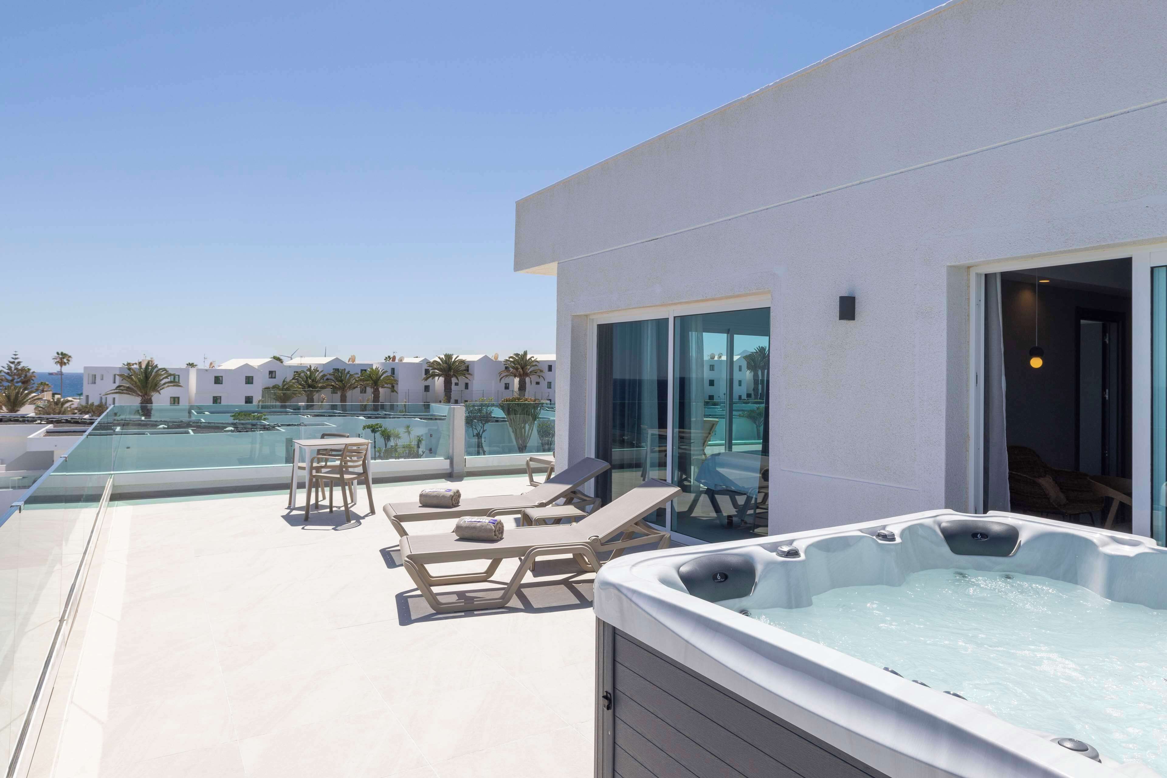 A rooftop terrace with a hot tub, lounge chairs, and a glass-enclosed pool area.