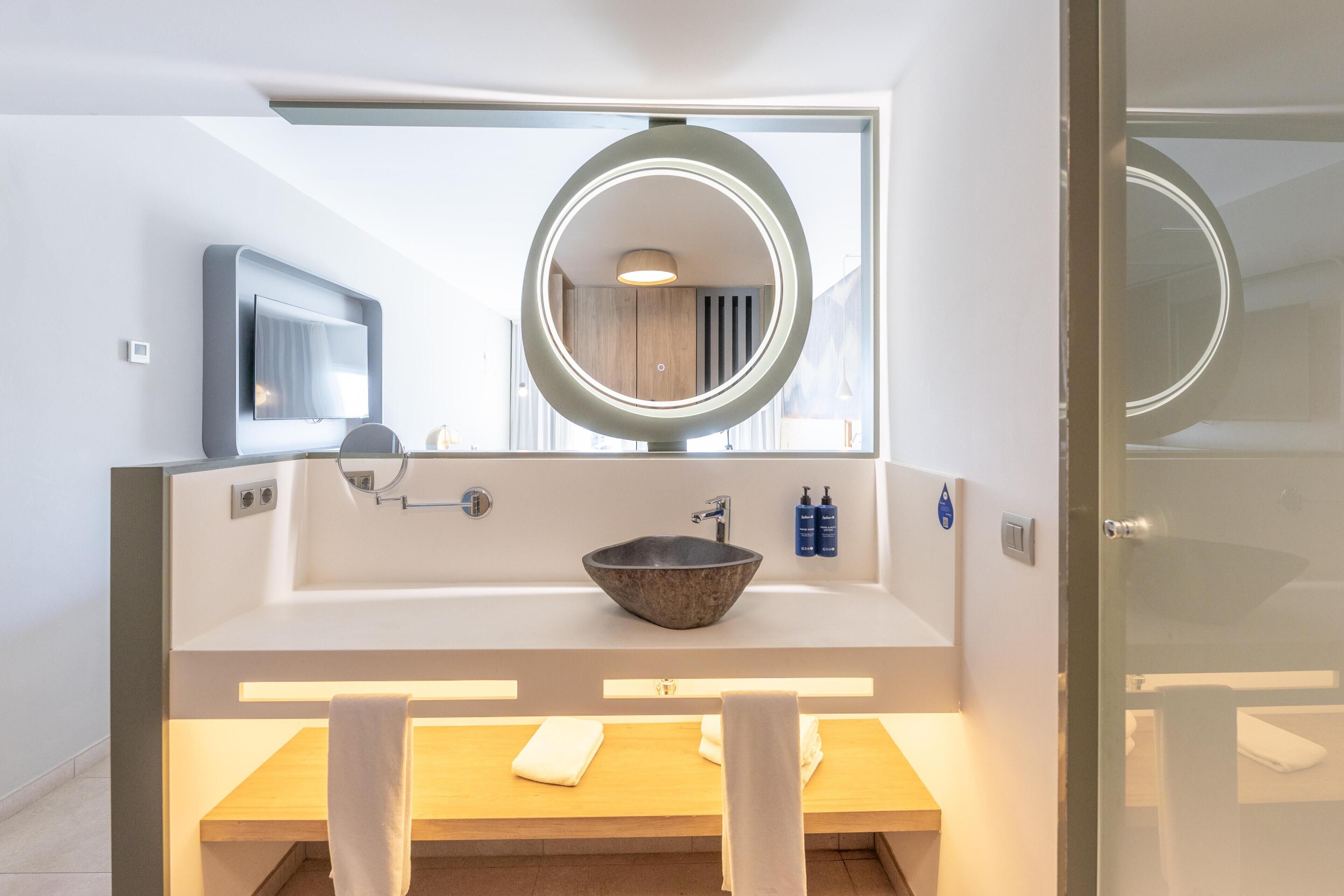 Un baño moderno con un espejo ovalado grande, un lavabo sobre encimera y un mueble de tocador de madera.