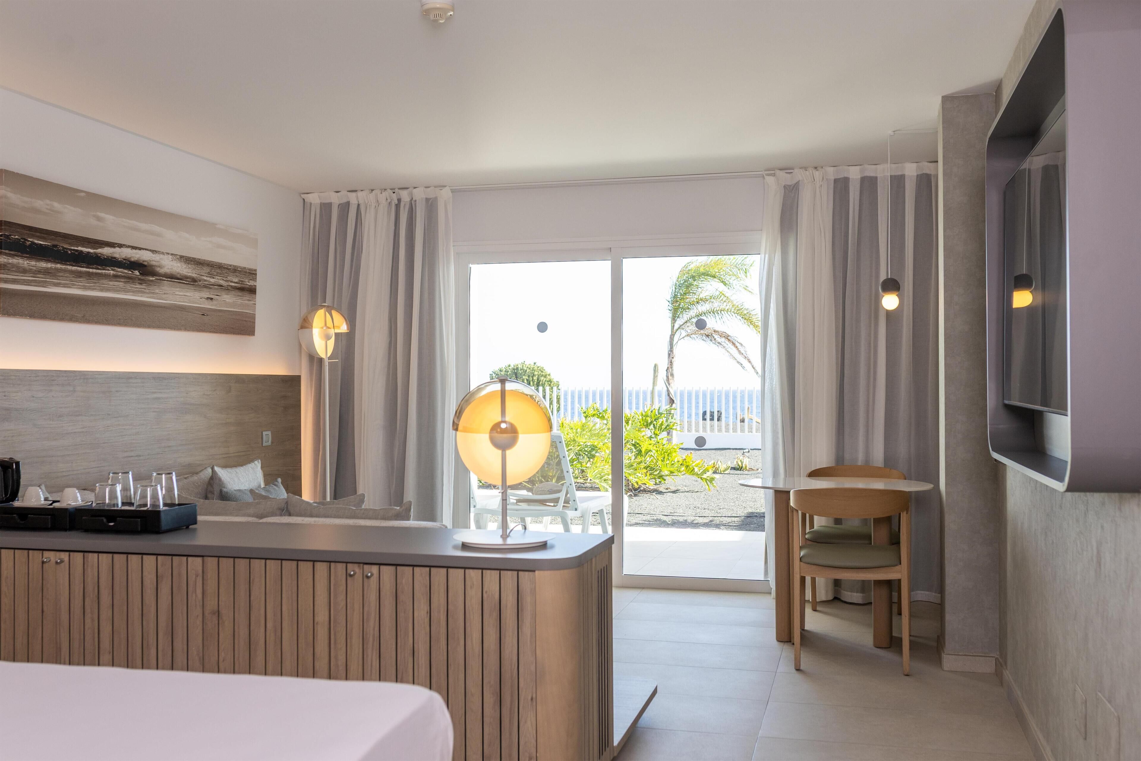 Habitación de hotel con cama, escritorio con lámpara, televisión y vista a la playa.