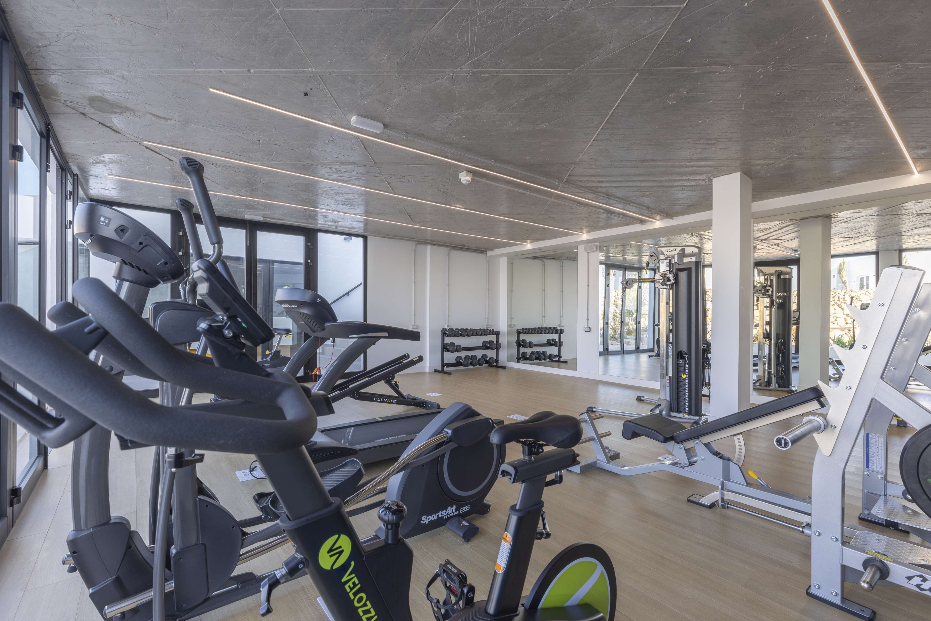 Un gimnasio con varios equipos de ejercicio, incluyendo cintas de correr y máquinas de pesas, y espejos en las paredes.
