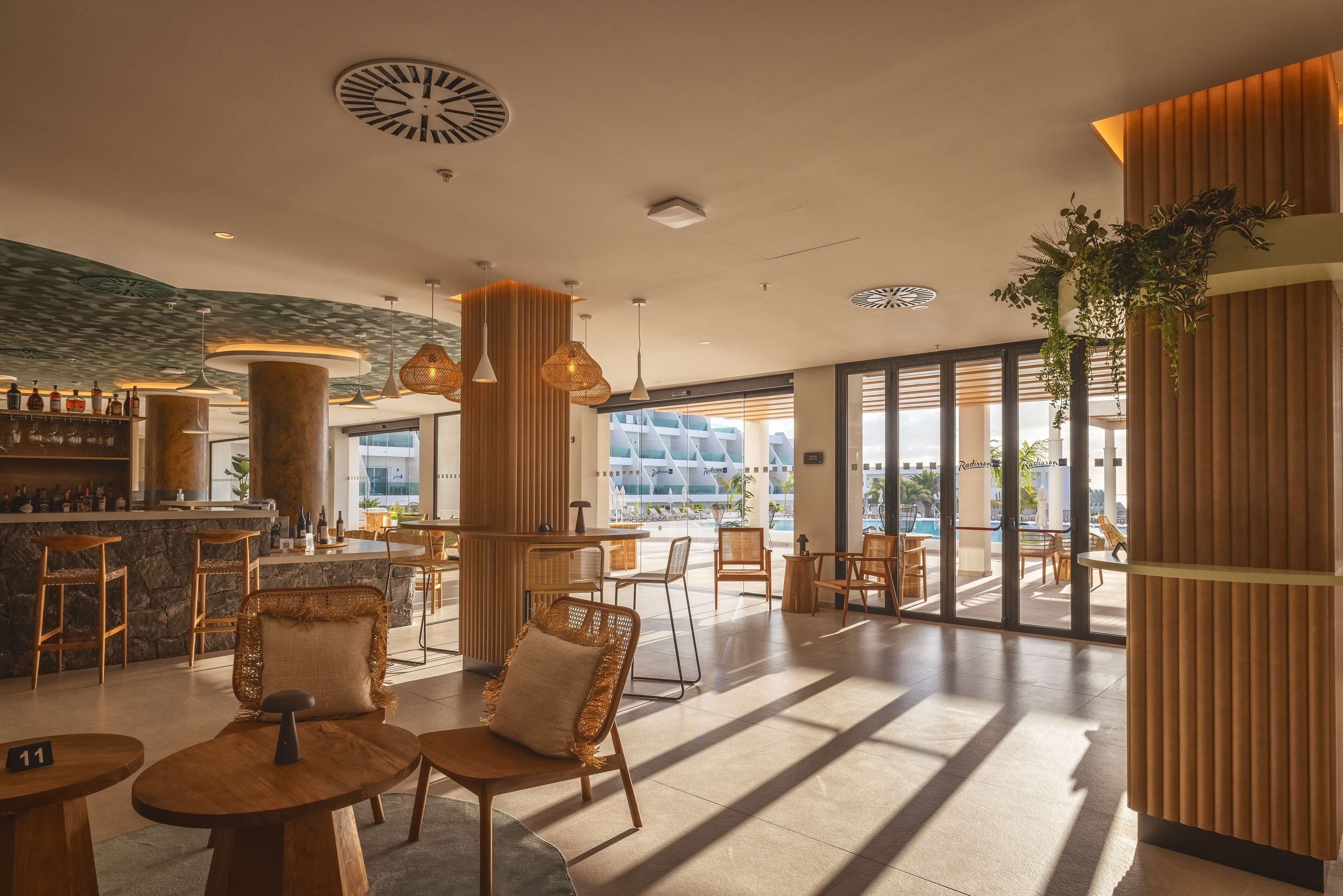 Un moderno vestíbulo de hotel con zona de bar, arreglos de asientos y grandes ventanales que ofrecen vistas al exterior.