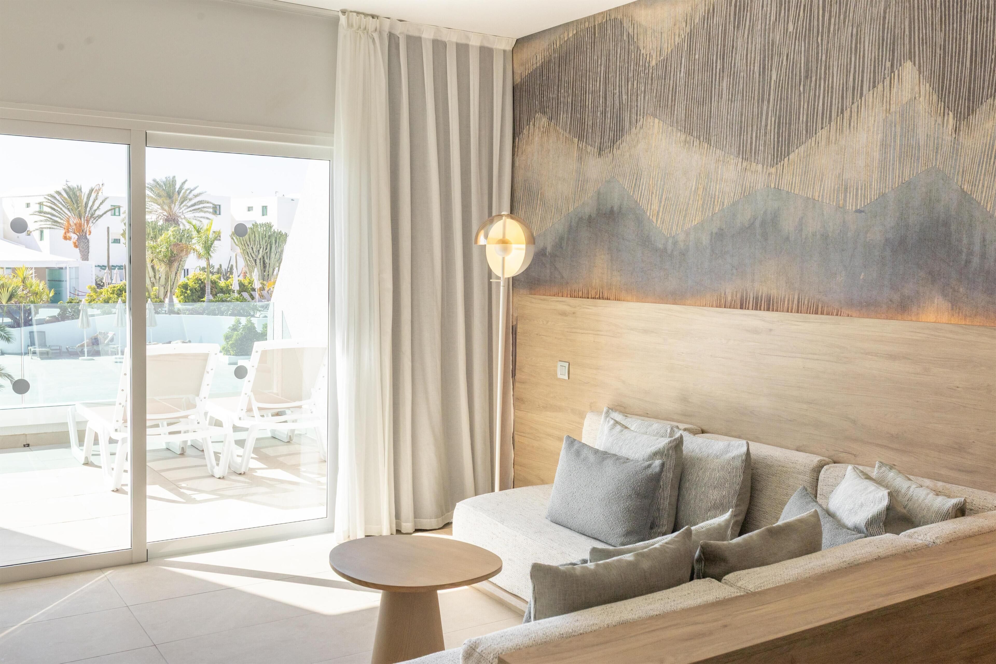Una habitación de hotel moderna con un sofá, una mesita redonda y un gran ventanal con cortinas.