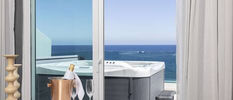 A balcony with a hot tub, a table with a champagne bottle and glasses, and a view of the ocean.