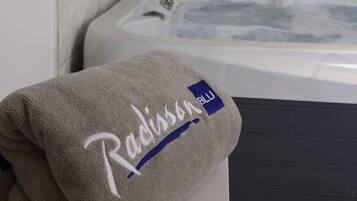 A bathroom with a marble wall, a white bathtub, and a towel with the Radisson Blu logo.