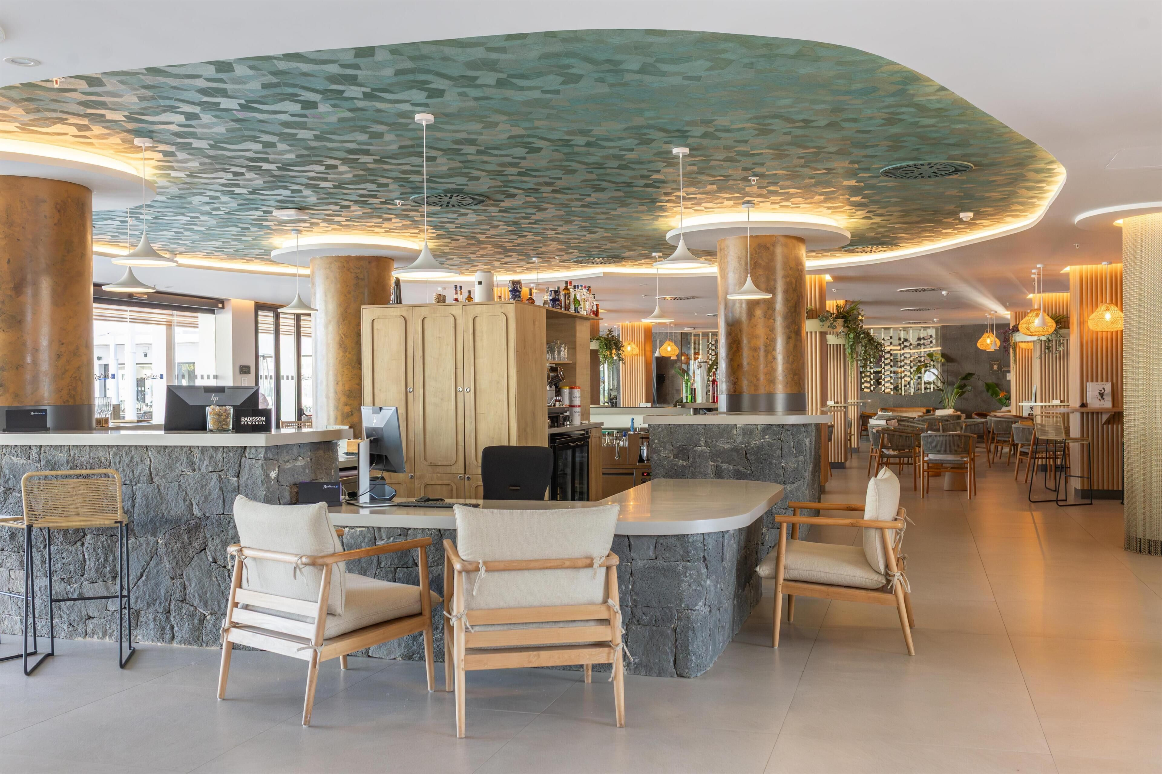 A modern hotel lobby with a curved ceiling, stone bar counter, and wooden chairs.