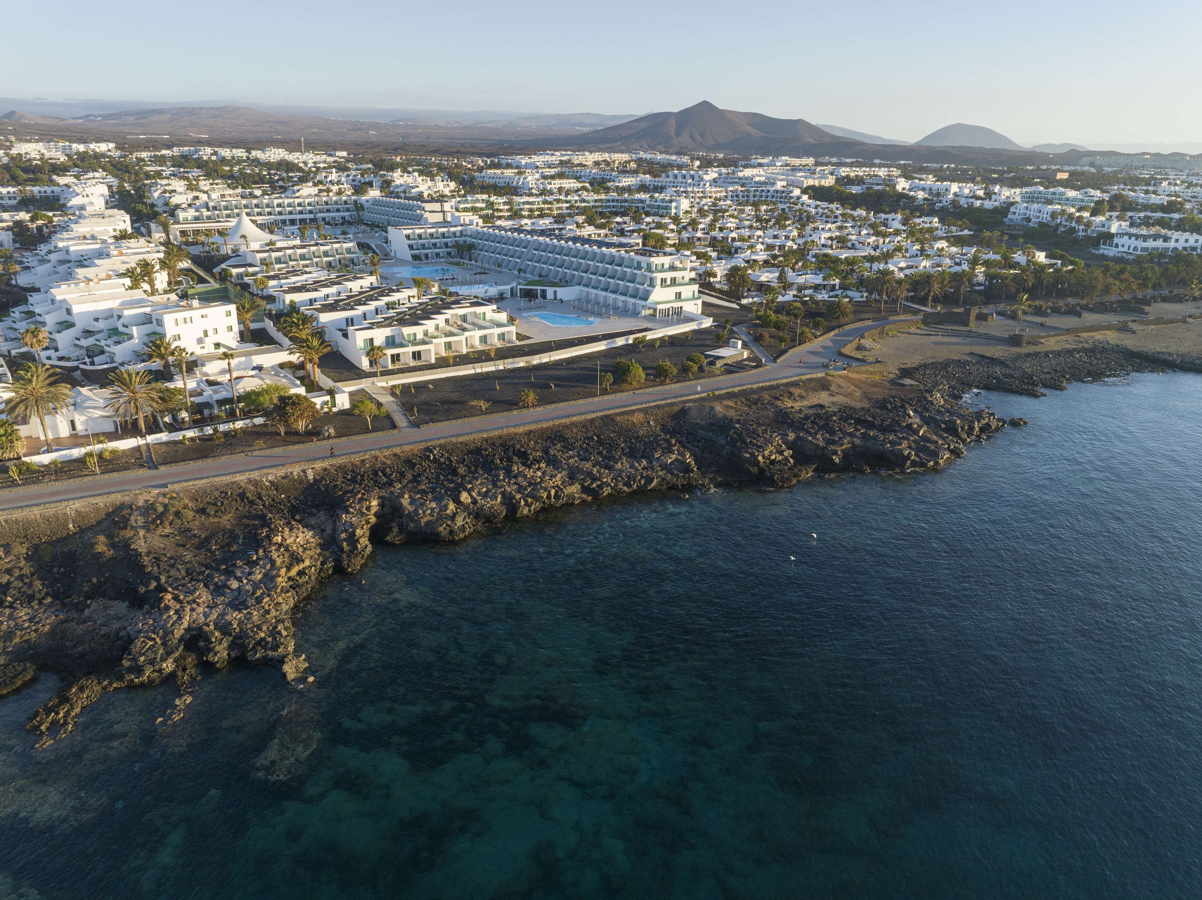 An aerial view of a coastal resort with white buildings, a rocky shoreline, and clear blue waters.