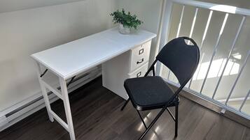 Ett litet, vitt skrivbord med en växt ovanpå, en svart stol och ett vitt element.