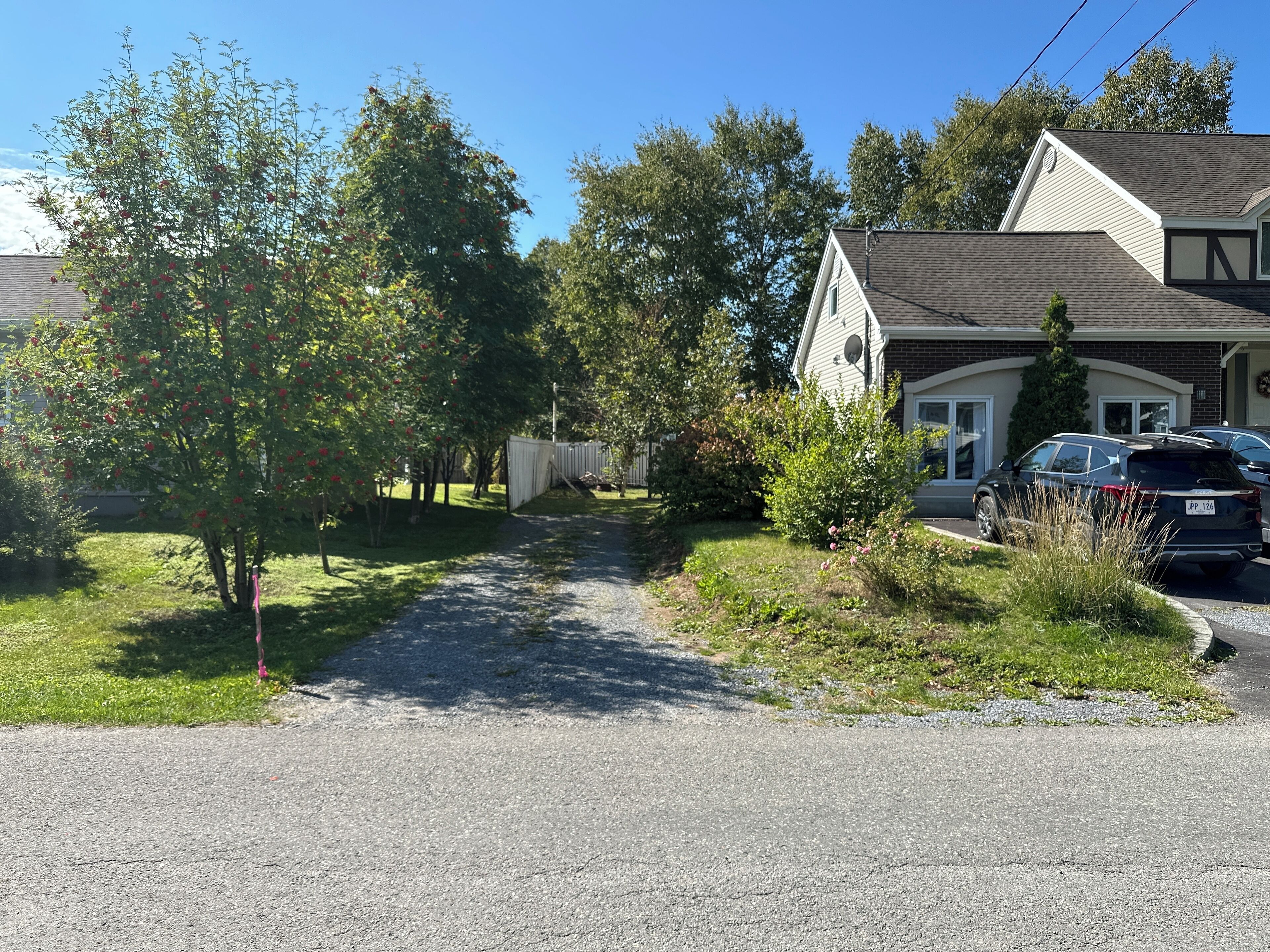 Une allée menant à une maison, avec un chemin de gravier, et la maison elle-même possède un toit en pente et un garage.