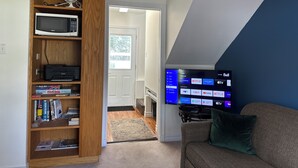 A living room with a flat-screen TV displaying various apps, a bookshelf with books and a microwave, and a couch with a pillow.