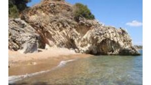 Línia de costa rocosa amb aigua cristal·lina i una platja de sorra.
