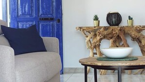 Un saló amb una porta blava, un sofà beix, una taula de centre rodona i un moble de consola de fusta amb objectes decoratius.