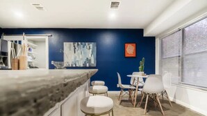 A modern kitchen with white cabinets, a marble countertop, and a dining area with white chairs and a small table.