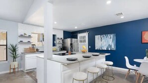 A modern kitchen with white cabinetry, a central island with stools, and a blue accent wall.