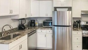 Una cocina con armarios blancos, electrodomésticos de acero inoxidable, un lavamanos y una encimera.