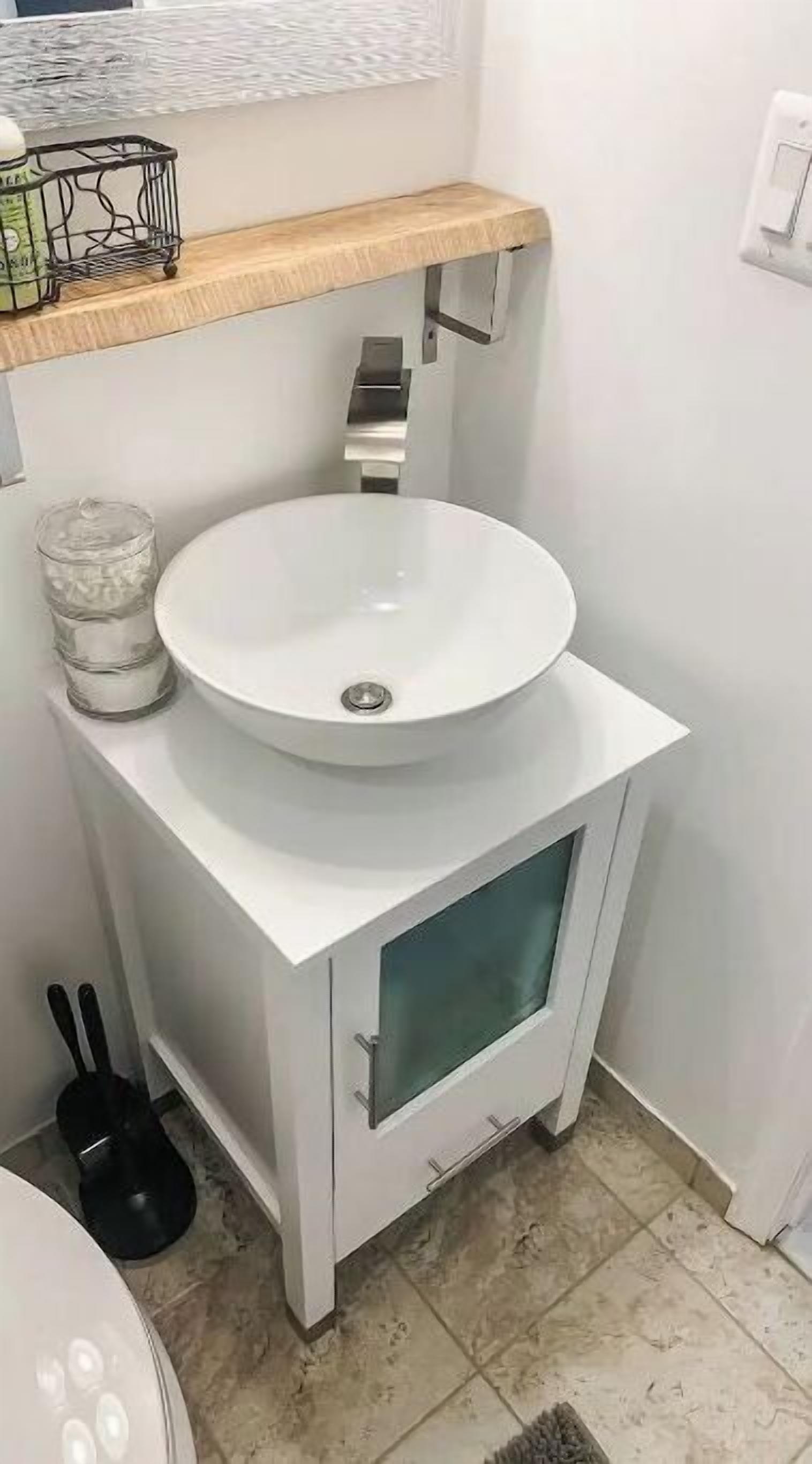 A bathroom with a white sink, a wooden shelf above it, and a glass-front cabinet below.