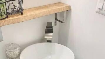 A bathroom with a white sink, a wooden shelf above it, and a glass-front cabinet below.