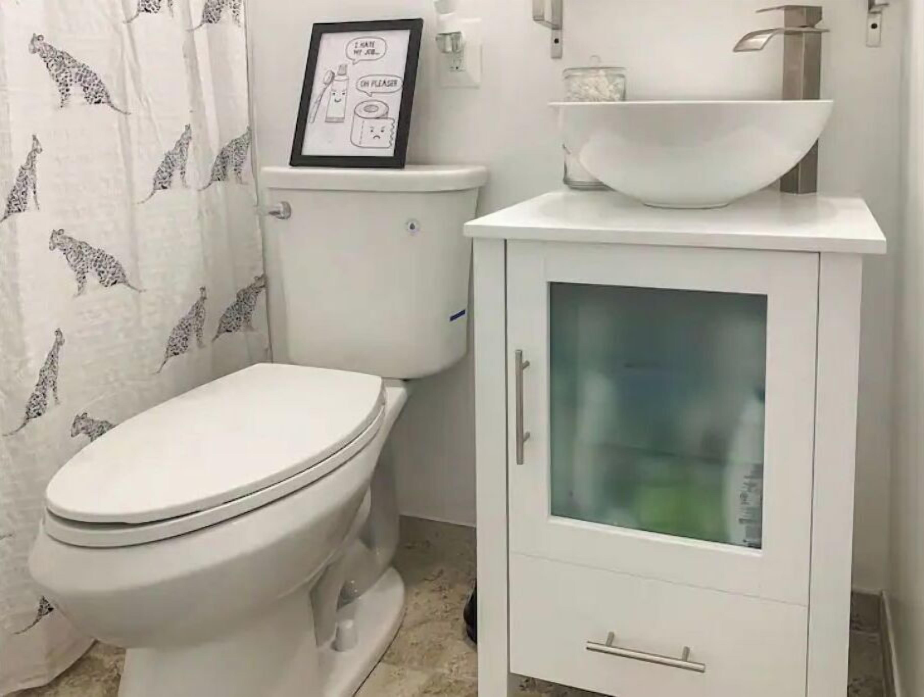 Un baño con inodoro, un armario con puerta de cristal y cortina de ducha con estampados de animales.