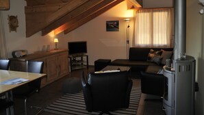 A cozy living room with a wooden ceiling, a fireplace, a sofa, a TV, and a dining area with a table and chairs. - Am Liimerweg by Interhome (Adelboden)