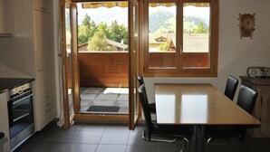 A kitchen with a wooden table and chairs, a stove, and a view of a mountain landscape through open doors. - Am Liimerweg by Interhome (Adelboden)