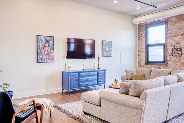 Un salon avec un téléviseur à écran plat, une commode bleue, un canapé beige et des œuvres d’art accrochées aux murs.