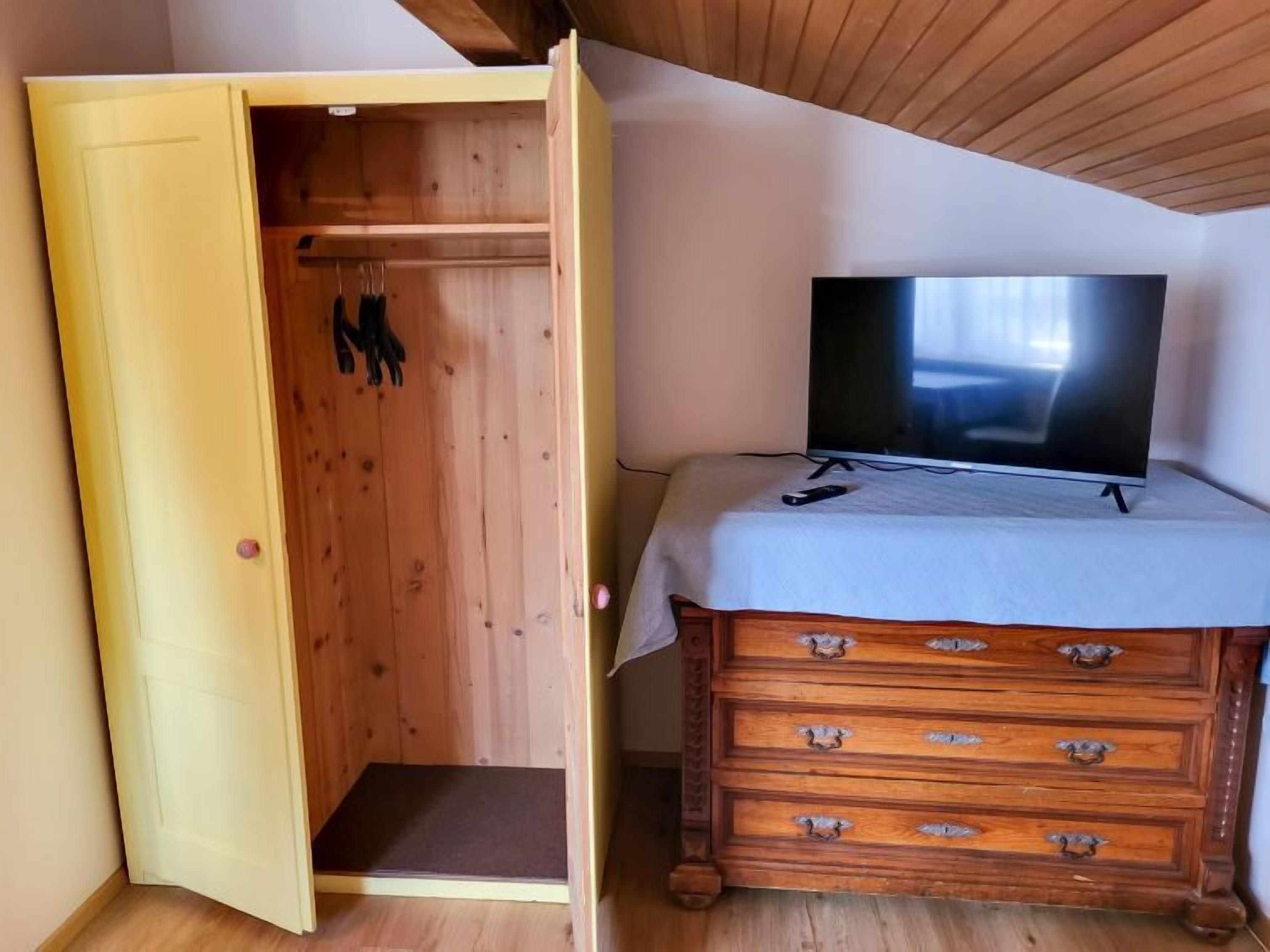 Quarto com guarda-roupa de madeira, televisão sobre uma mesa e um degrau pequeno que dá para um closet.