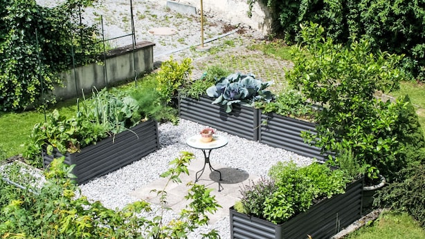 A garden patio with a round table and benches, surrounded by raised planters and a gravel path. - Apartment Frieda by Interhome (Landeck)